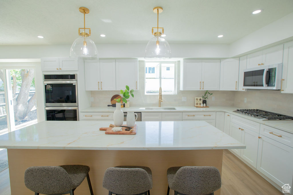 Kitchen featuring a sink, stainless steel appliances, a breakfast bar area, backsplash, and white cabinets