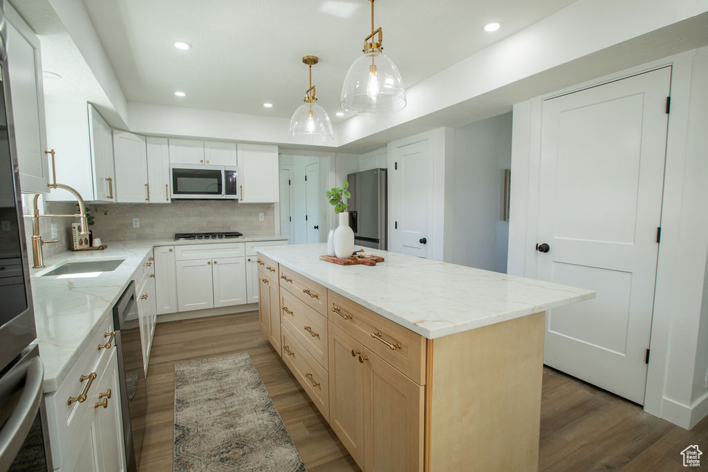 Kitchen featuring stainless steel appliances, a sink, wood finished floors, a center island, and decorative backsplash