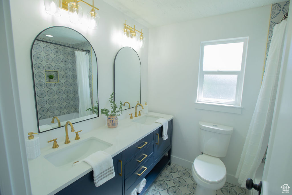 Full bathroom featuring toilet, double vanity, a shower with curtain, and baseboards
