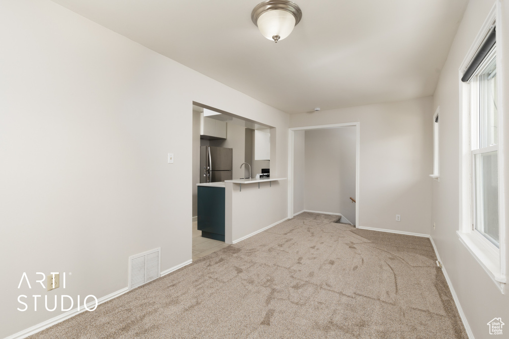 Unfurnished living room featuring a wealth of natural light, visible vents, a sink, and light carpet