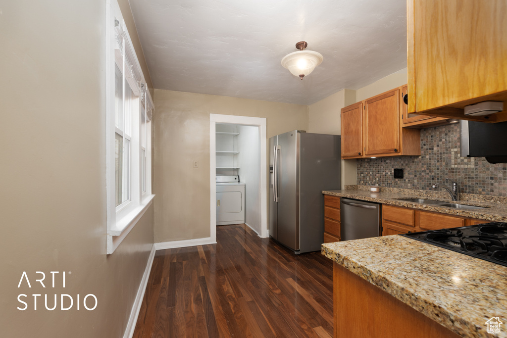 Kitchen featuring baseboards, a sink, washer / dryer, backsplash, and stainless steel appliances