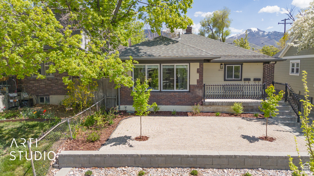 View of front of property with a mountain view, a chimney, fence, brick siding, and roof with shingles