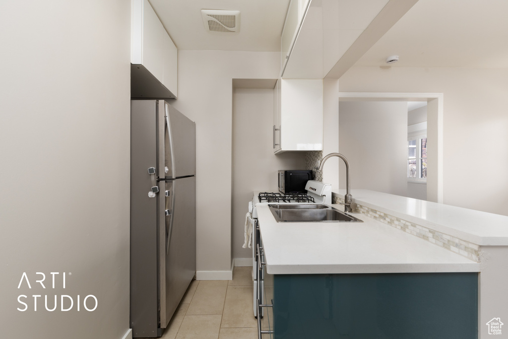 Kitchen featuring freestanding refrigerator, visible vents, light tile patterned flooring, light countertops, and white cabinets