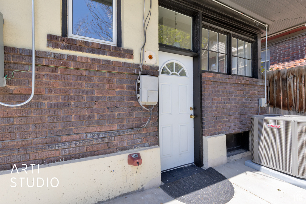 View of exterior entry featuring brick siding, fence, and central AC