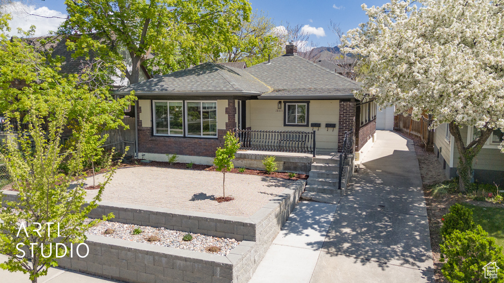 View of front of home featuring covered porch, roof with shingles, fence, brick siding, and driveway