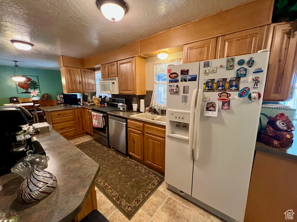 Kitchen featuring a textured ceiling, a wealth of natural light, white appliances, and a sink
