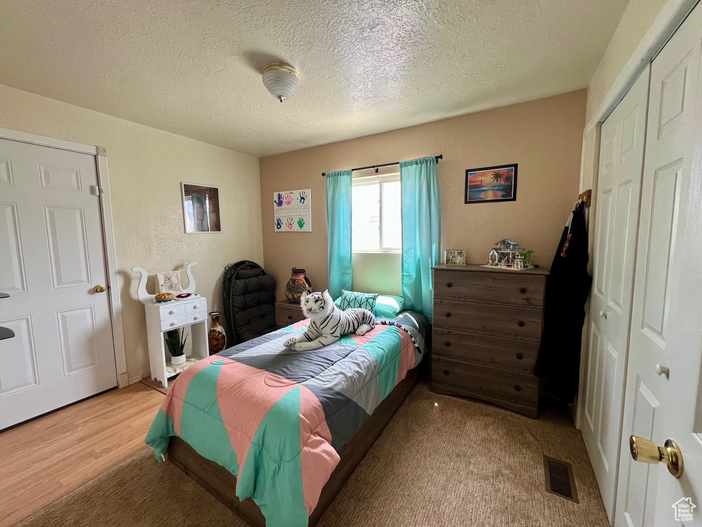 Bedroom featuring a closet, a textured ceiling, visible vents, and light wood-style floors