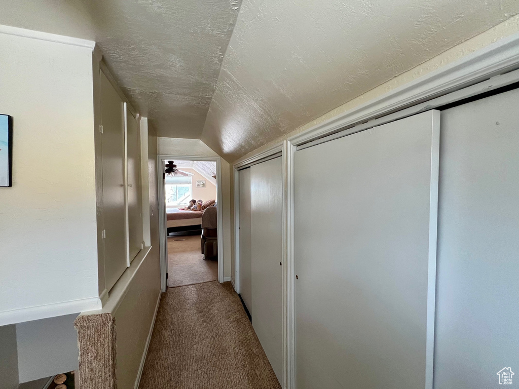 Hall featuring a textured ceiling, lofted ceiling, and carpet floors
