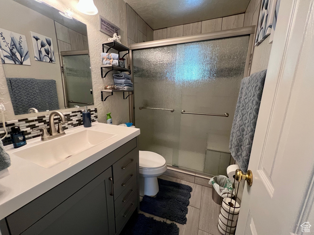 Full bath with toilet, a shower stall, backsplash, a textured wall, and vanity