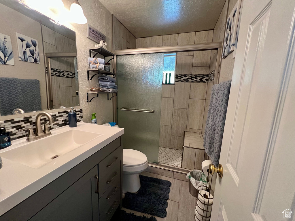 Full bathroom featuring a shower stall, vanity, tasteful backsplash, and a textured wall