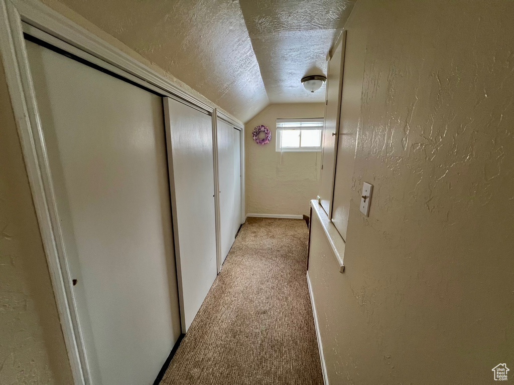 Corridor with a textured ceiling, baseboards, a textured wall, light carpet, and lofted ceiling