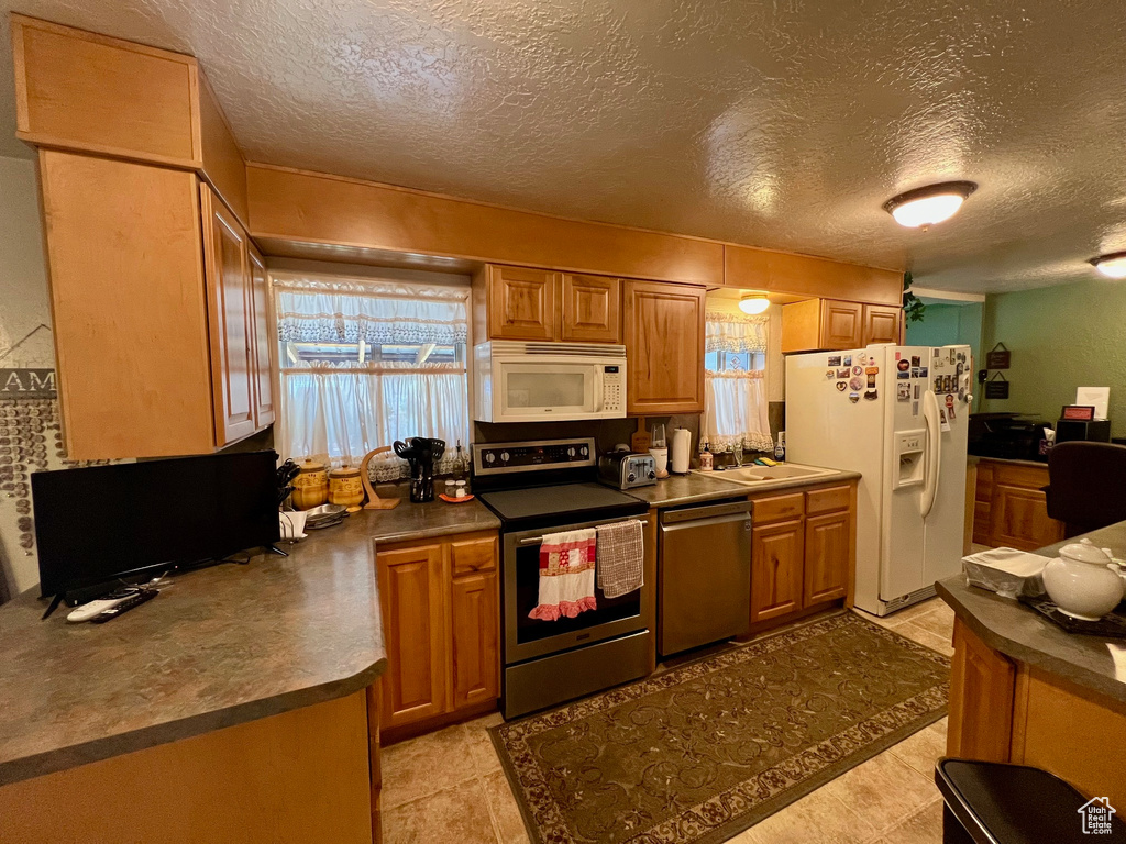 Kitchen featuring dark countertops, appliances with stainless steel finishes, brown cabinets, and a textured ceiling