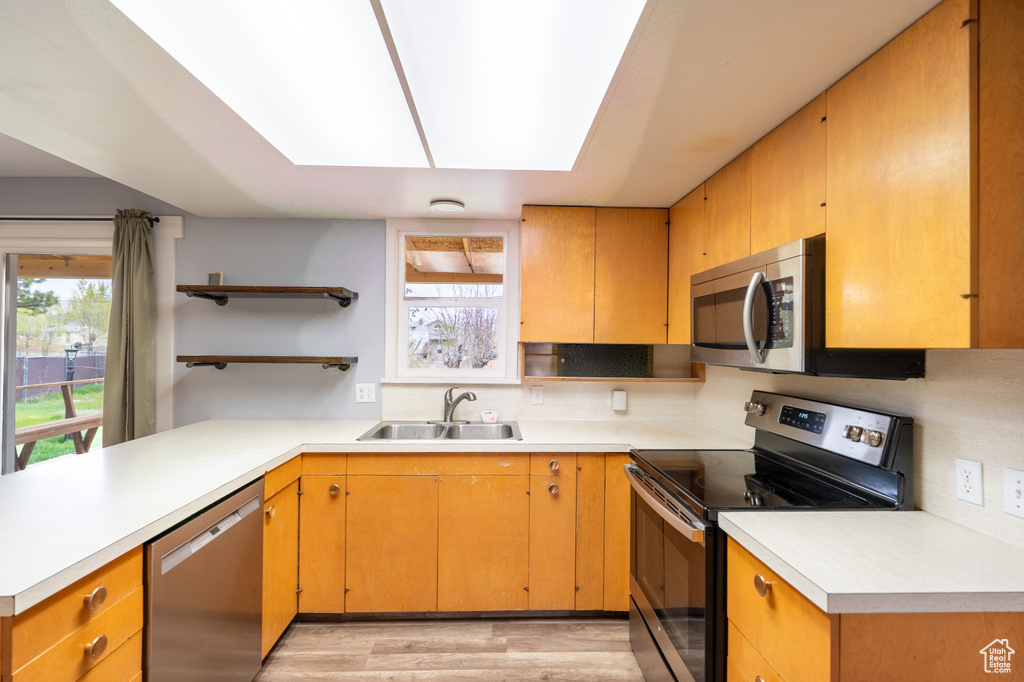 Kitchen featuring a sink, open shelves, light wood-style flooring, decorative backsplash, and appliances with stainless steel finishes