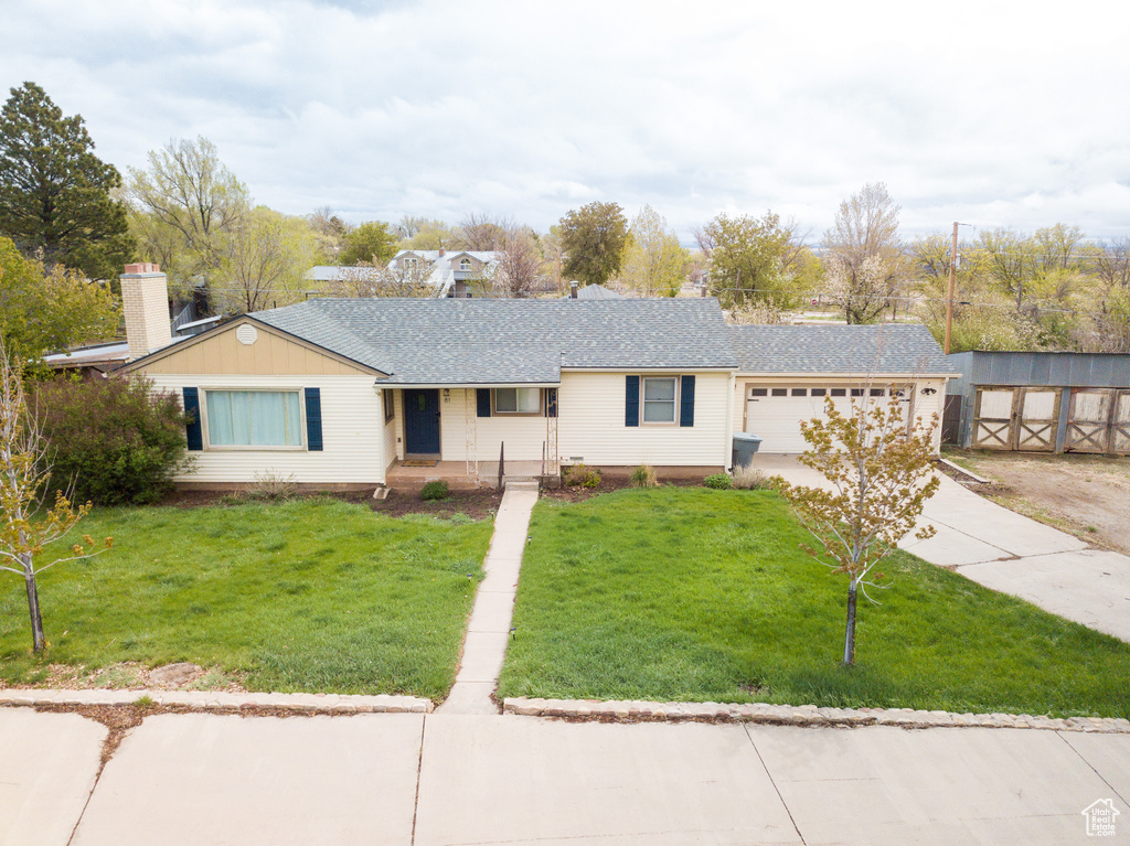 Single story home featuring covered porch, an attached garage, driveway, a front yard, and a shingled roof