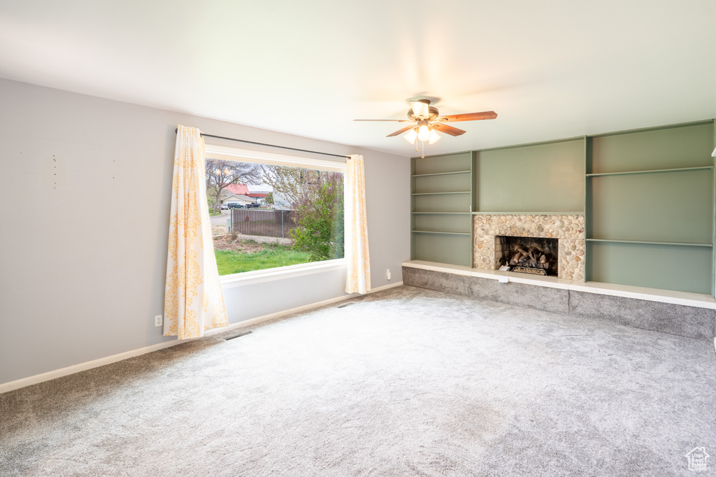 Unfurnished living room featuring a fireplace, carpet floors, visible vents, baseboards, and ceiling fan