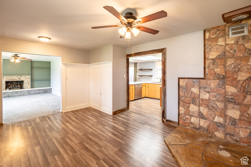 Empty room featuring a sink, wood finished floors, a fireplace with raised hearth, a ceiling fan, and baseboards