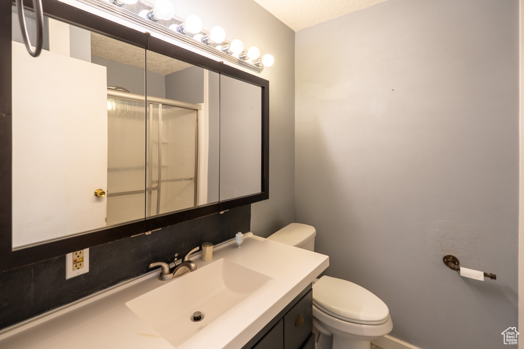 Full bathroom featuring a shower with door, toilet, a textured ceiling, and vanity