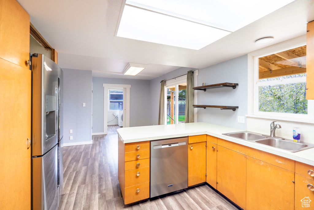 Kitchen featuring appliances with stainless steel finishes, a sink, a peninsula, light countertops, and light wood-type flooring