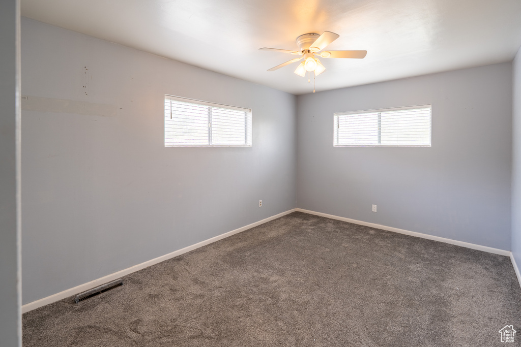 Carpeted spare room featuring baseboards, a wealth of natural light, visible vents, and ceiling fan