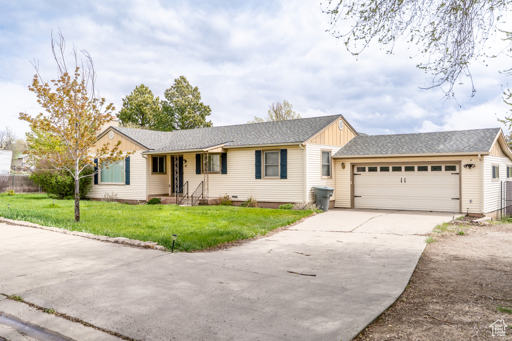 Ranch-style home with an attached garage, concrete driveway, board and batten siding, a front yard, and roof with shingles