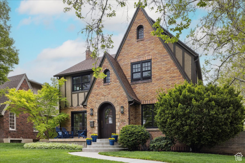 English style home featuring a chimney, a front yard, brick siding, and a shingled roof