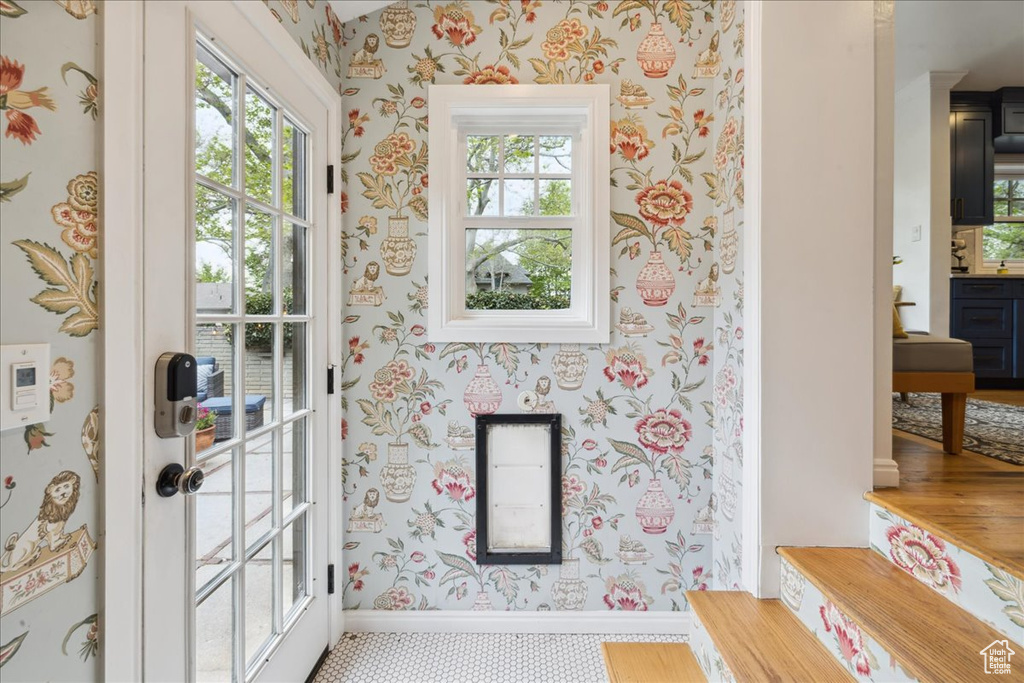 Doorway with wallpapered walls, baseboards, and a healthy amount of sunlight