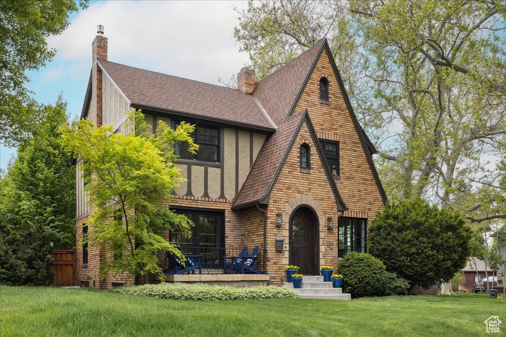 View of front of house featuring brick siding, a shingled roof, a chimney, and a front yard