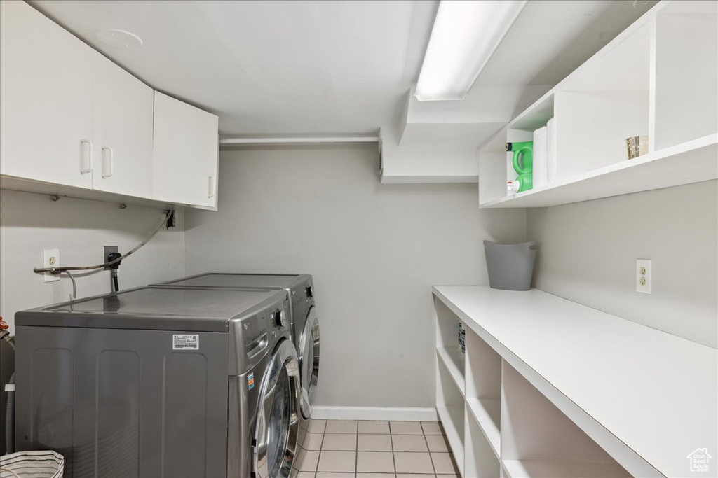 Laundry area with separate washer and dryer, cabinet space, baseboards, and light tile patterned floors