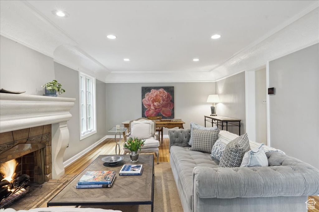 Living room featuring ornamental molding, recessed lighting, a fireplace, light wood-style flooring, and baseboards