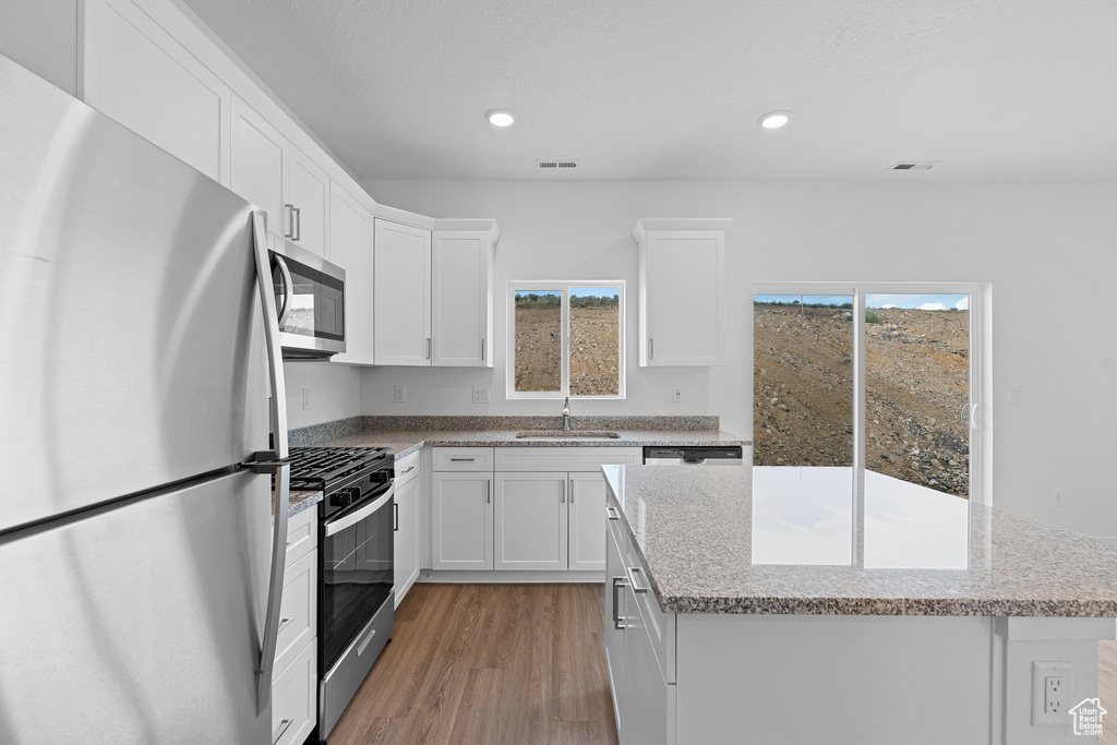 Kitchen with a center island, light wood-style flooring, a sink, stainless steel appliances, and white cabinets