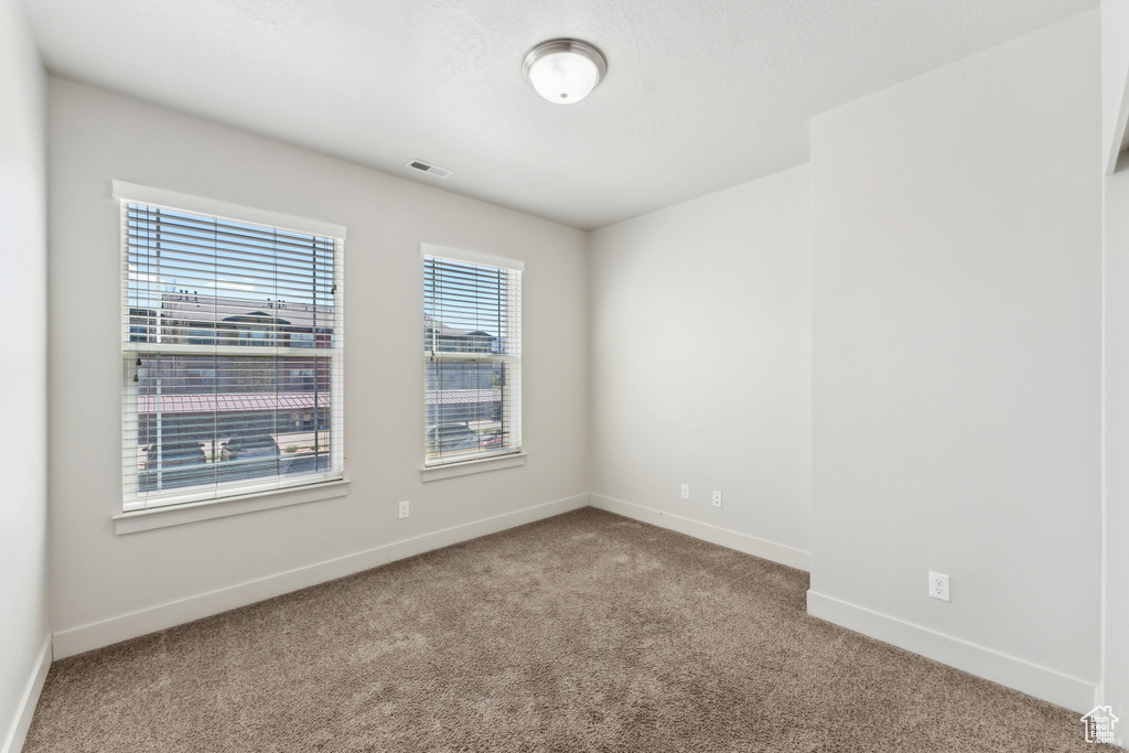 Empty room with carpet flooring, visible vents, and baseboards