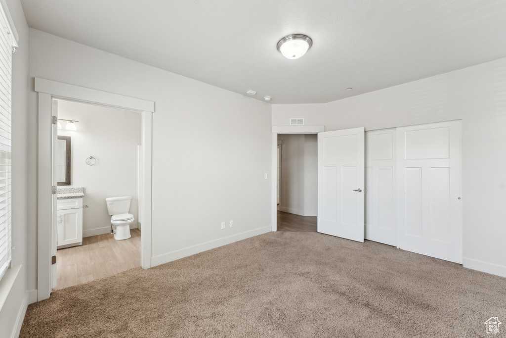 Unfurnished bedroom with a closet, baseboards, carpet flooring, visible vents, and connected bathroom