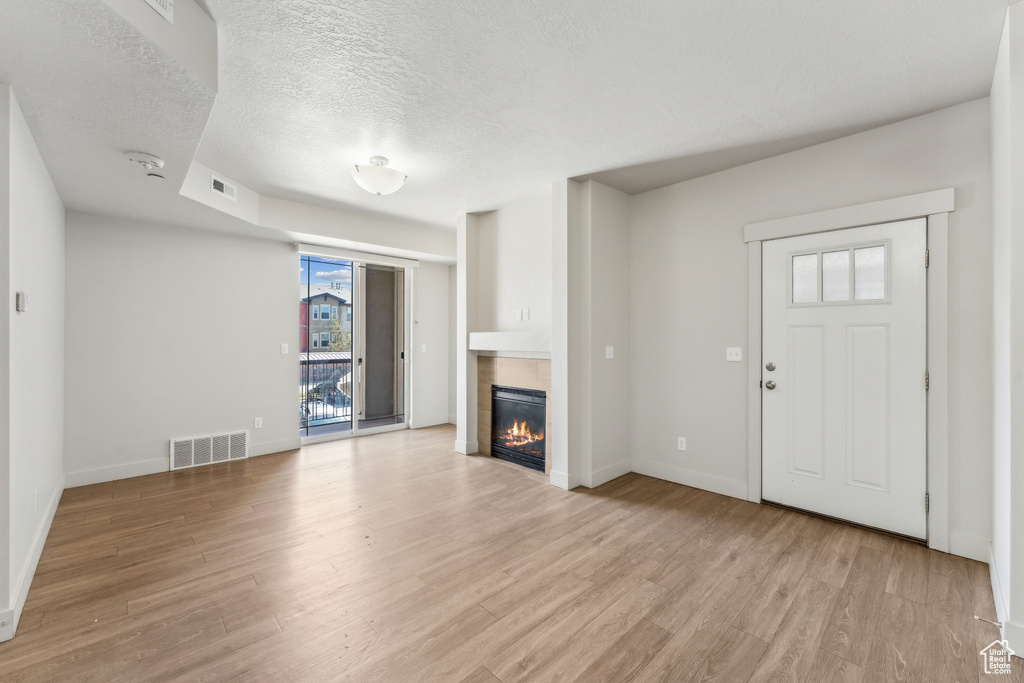 Unfurnished living room with a tiled fireplace, visible vents, light wood-style flooring, and a textured ceiling