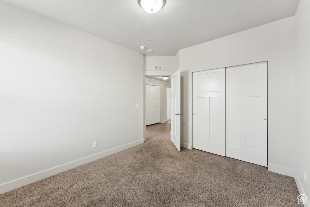 Unfurnished bedroom featuring carpet floors, baseboards, visible vents, and a closet