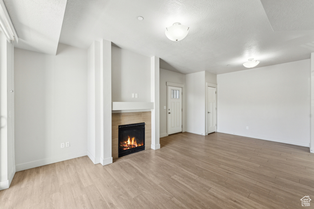 Unfurnished living room featuring light wood finished floors, a textured ceiling, a tiled fireplace, and baseboards