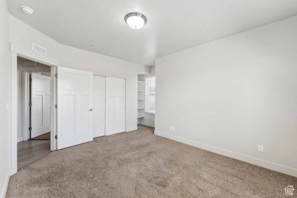 Unfurnished bedroom with baseboards, carpet floors, a closet, and visible vents