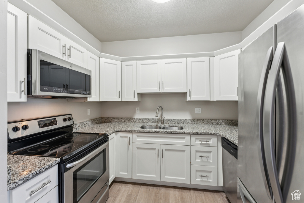 Kitchen featuring light stone countertops, light wood-style flooring, a sink, white cabinetry, and appliances with stainless steel finishes