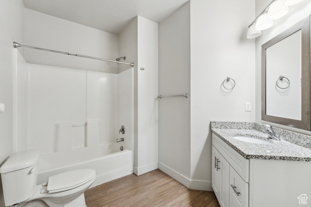 Full bath with shower / bath combination, toilet, baseboards, vanity, and wood finished floors