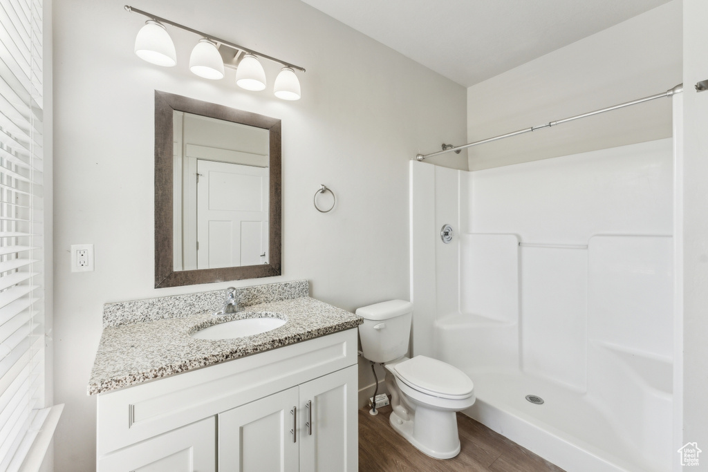 Bathroom featuring toilet, a shower, wood finished floors, and vanity