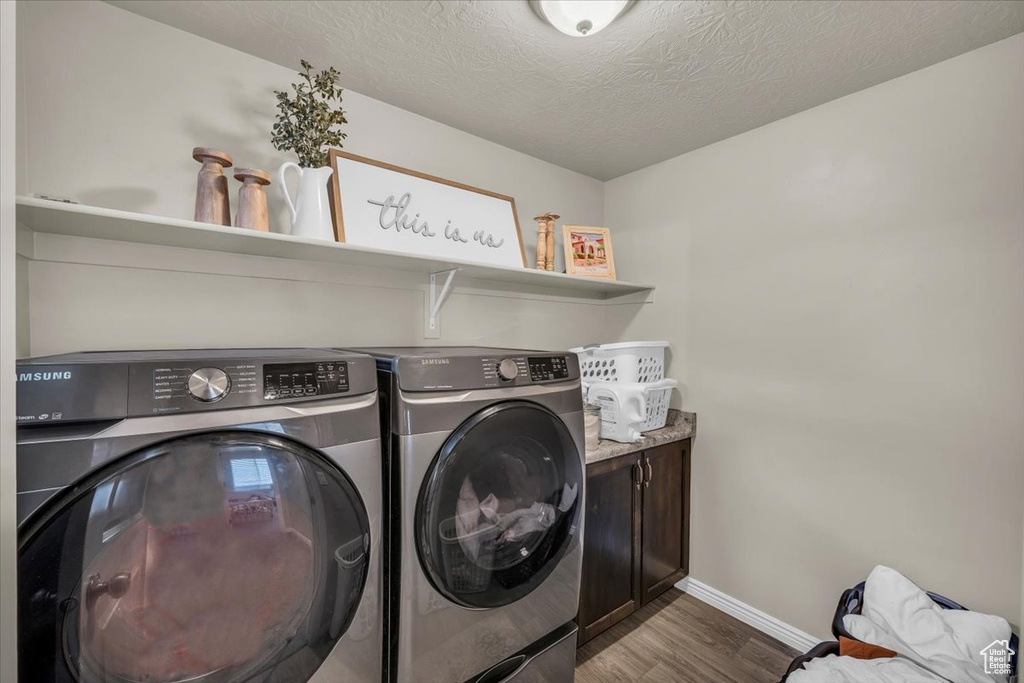 Laundry area with cabinet space, a textured ceiling, dark wood-type flooring, baseboards, and independent washer and dryer