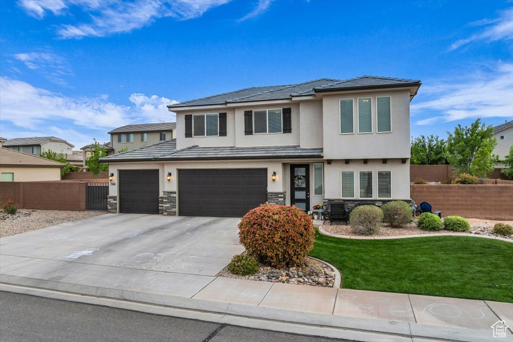 Prairie-style home with fence, an attached garage, driveway, stucco siding, and a front yard