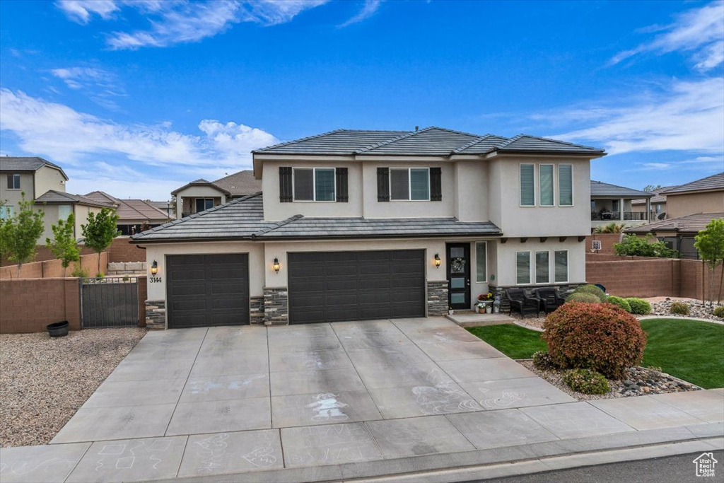View of front facade featuring fence, stone siding, concrete driveway, a garage, and stucco siding
