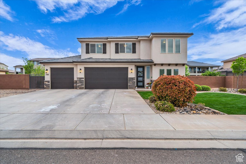 Prairie-style house with a tile roof, fence, stucco siding, and driveway