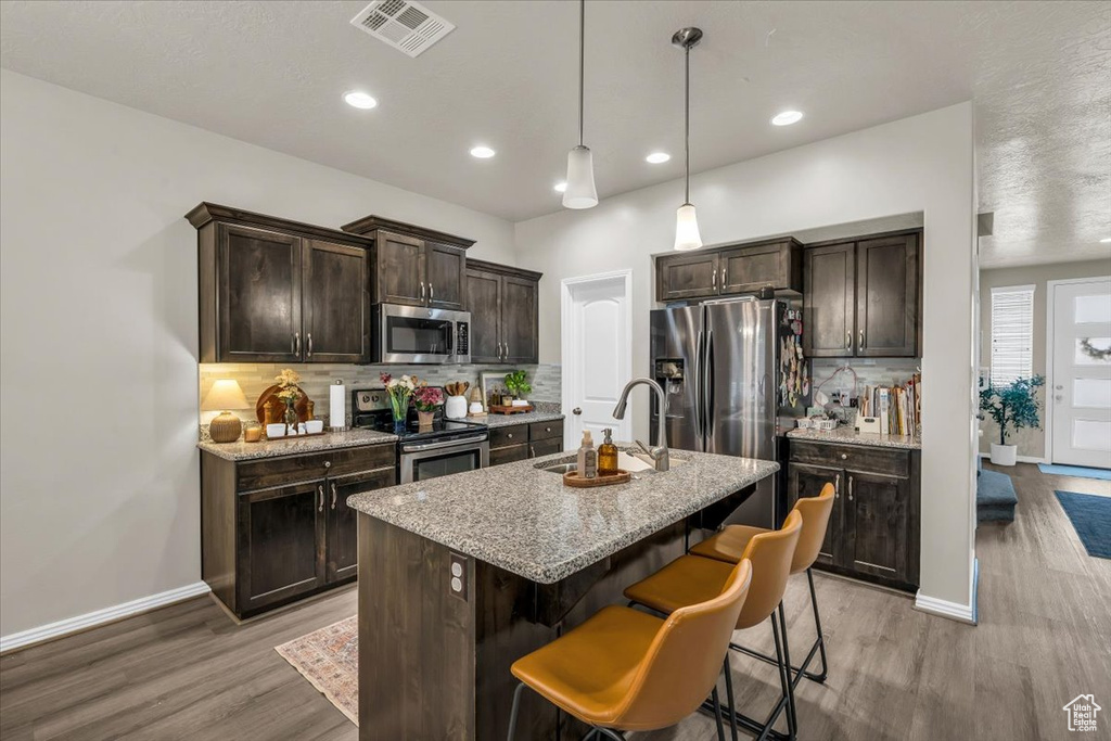 Kitchen with a breakfast bar, visible vents, a sink, dark brown cabinetry, and appliances with stainless steel finishes