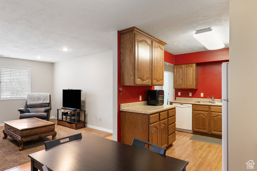 Kitchen with a sink, white appliances, brown cabinets, open floor plan, and light countertops