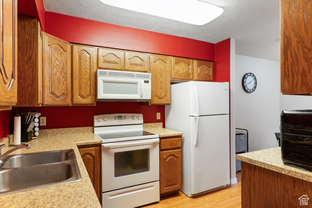 Kitchen with white appliances, a sink, light wood-type flooring, light countertops, and brown cabinetry