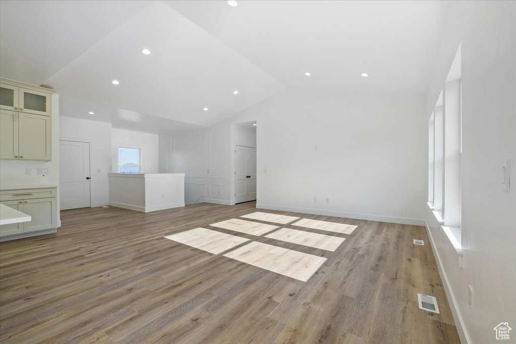 Unfurnished living room with vaulted ceiling, light wood-type flooring, visible vents, and recessed lighting