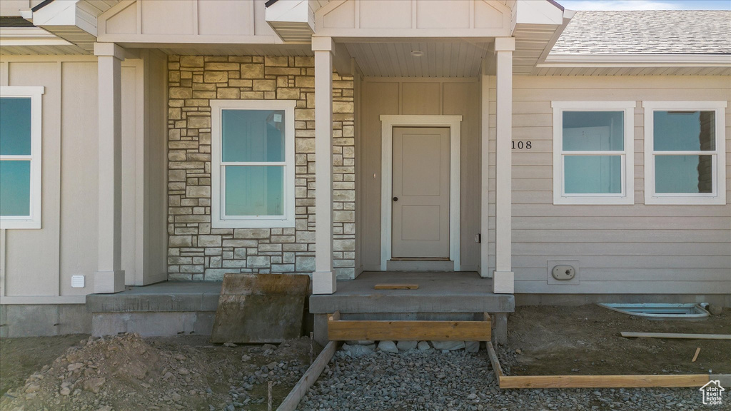 Property entrance with stone siding, a shingled roof, and board and batten siding