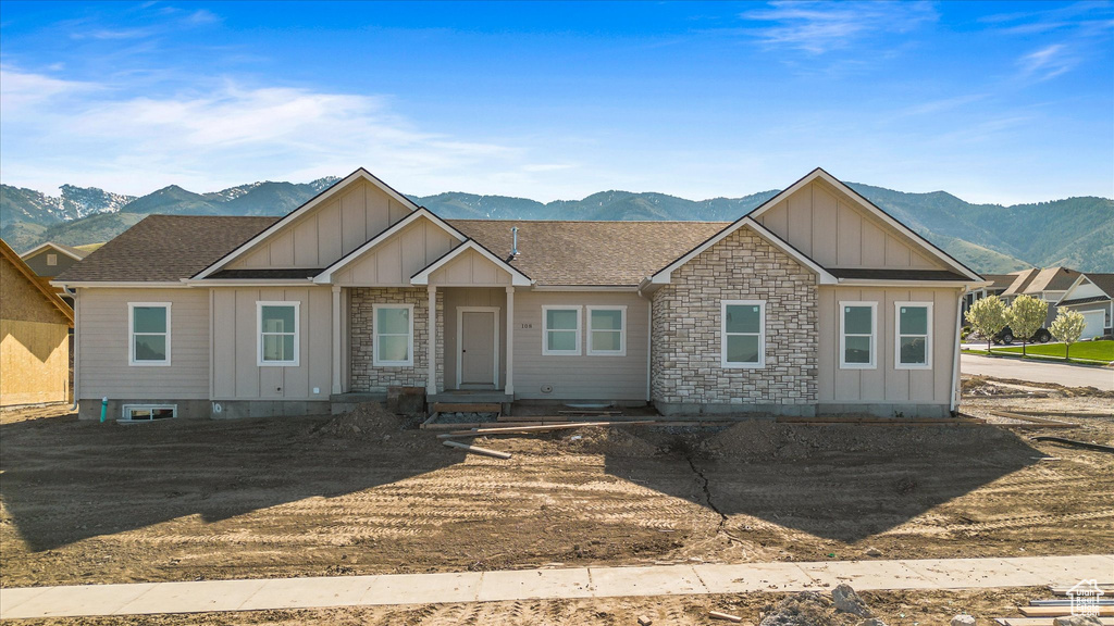 View of front facade featuring roof with shingles, stone siding, a mountain view, and board and batten siding