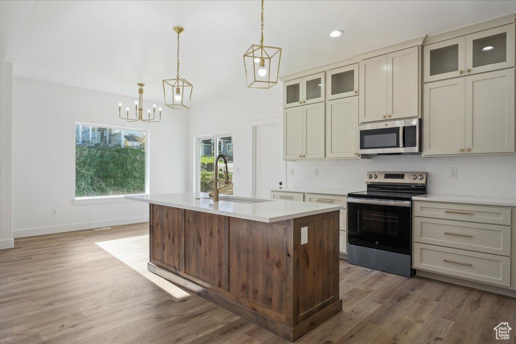 Kitchen featuring a sink, light wood-type flooring, an inviting chandelier, light countertops, and appliances with stainless steel finishes